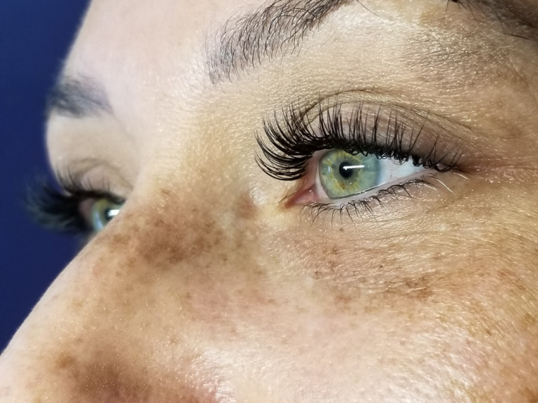 Hybrid Lash Extensions Close-up of a woman's eyes with long lashes and green irises, showing freckles on her skin.